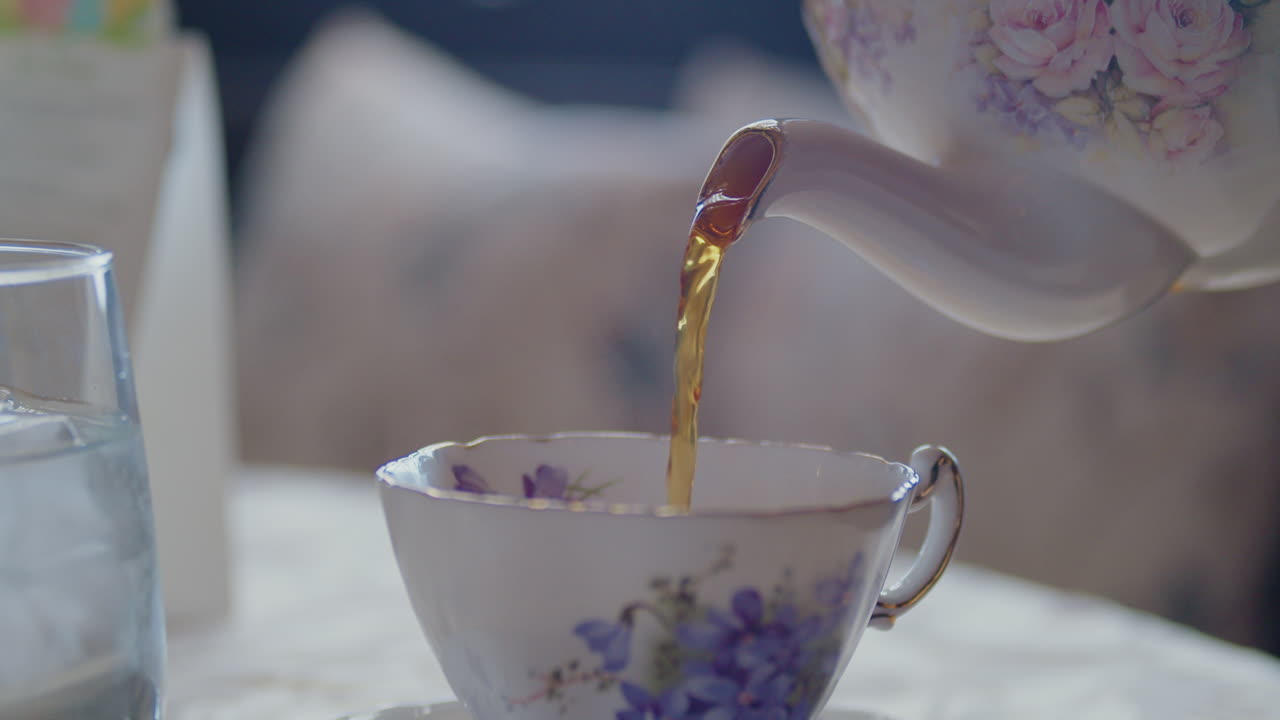 창문에 켜진 황금 으로 된 차 비는 아름다운 보라색 꽃 컵에 부어집니다.