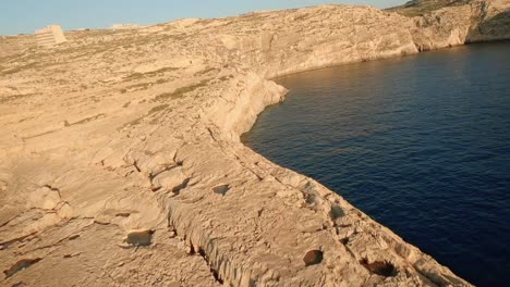 Un-Dron-Aéreo-Explora-La-Escarpada-Costa-De-La-Bahía-De-Dwejra-Y-Revela-Rocas-De-Colores-Deslumbrantes-Bañadas-Por-La-Luz-Dorada-Del-Atardecer.