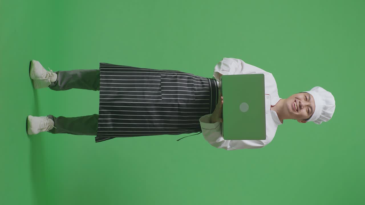 Full Body Of Asian Man Chef Using A Laptop And Smiling To Camera While Standing In The Green Screen Background Studio