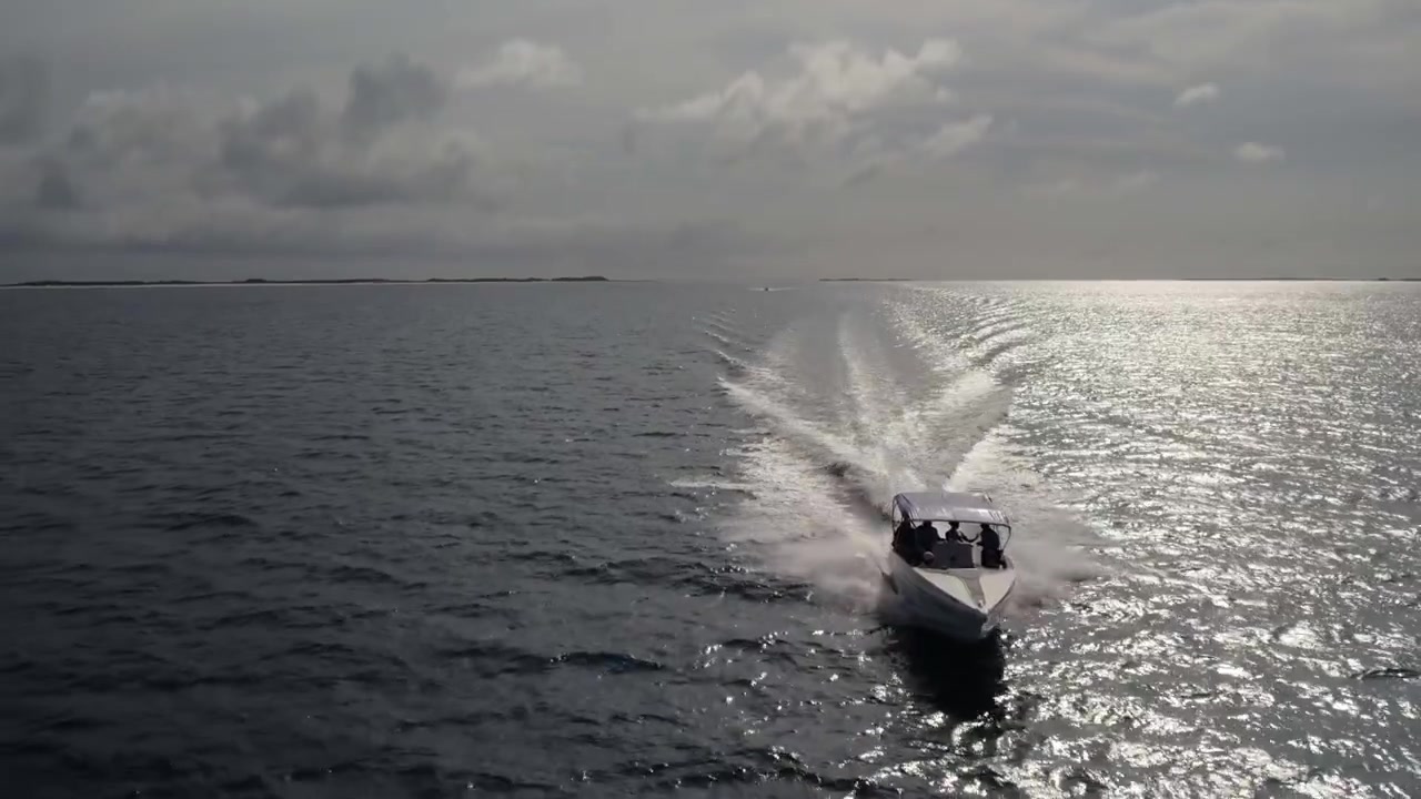 Perahu cepat mendekat di atas perairan terbuka dengan pantulan matahari dan cakrawala jauh terlihat