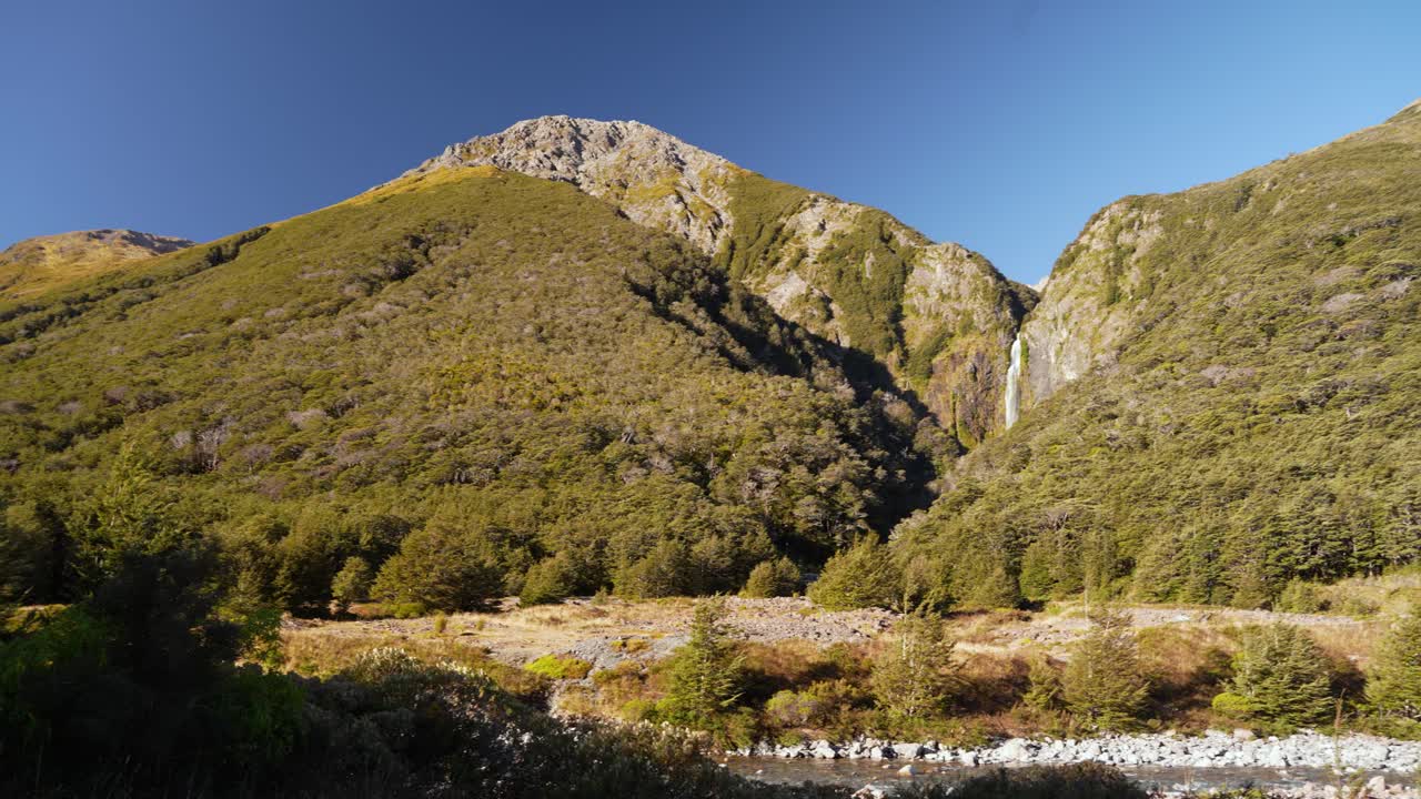 Sunset lighting on Devils Punchbowl waterfall cascading through lush forest terrain, estabilshing pan