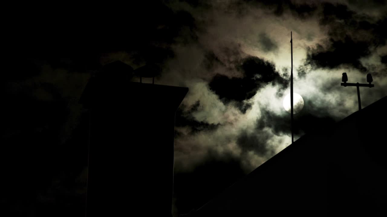 4k Very fast Time lapse of nightsky with clouds moving and moon shining, revealing the silhouette of a building