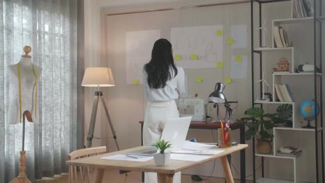 asian woman designer looking at the design sketch paper on the wall