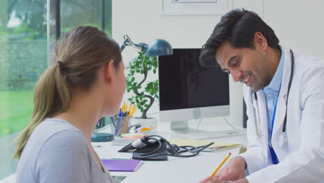 Male-Doctor-Or-GP-In-Appointment-With-Teenage-Girl-Making-Notes-On-Clipboard