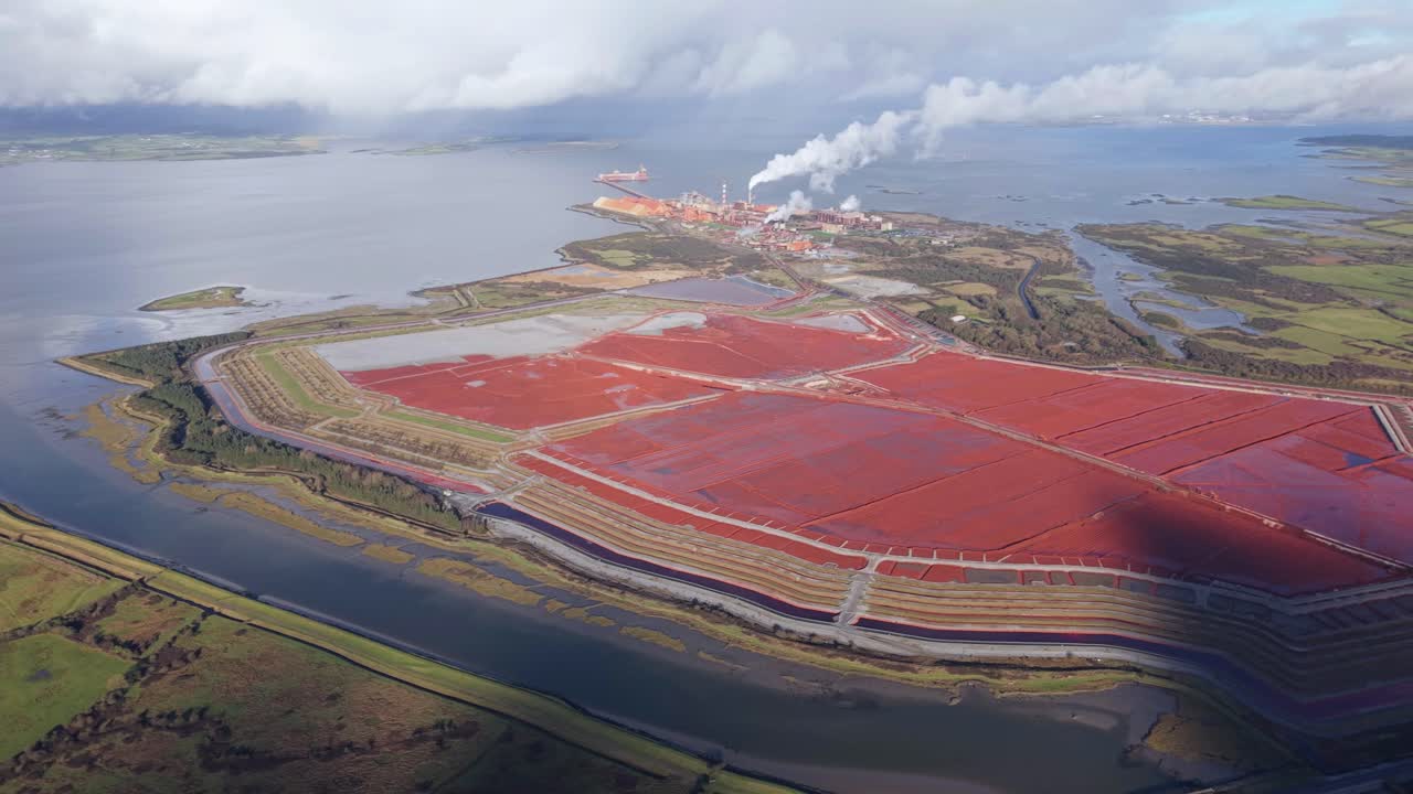 Red Sludge Pond Of Aughinish Alumina Refinery On Shannon Estuary In County Limerick, Ireland. aerial panning shot