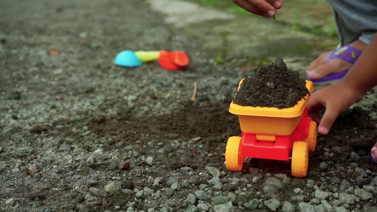 manos de un niño feliz jugando con piedras, arena y juguetes de camión en la carretera