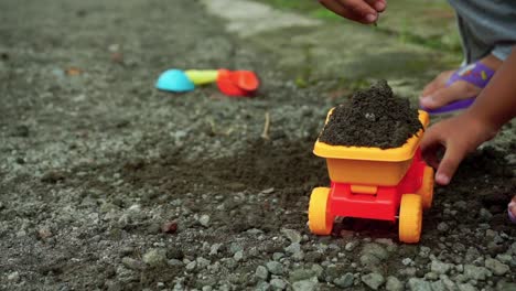 hands of a happy kid playing with stone, sand and truck toys on the road