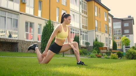 a young woman with headphones is stretching on the grass in a city park in slow motion. listen to music while playing sports