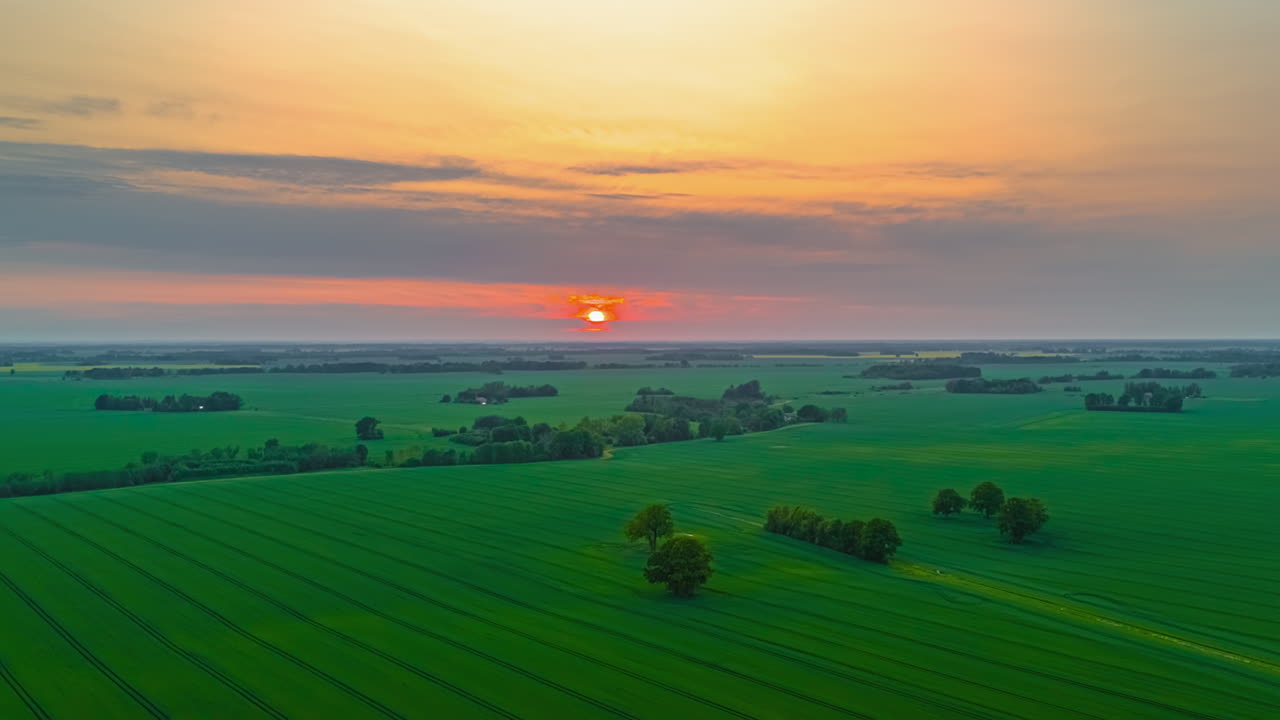 Sun disappearing below horizon over lush green fields in drone hyperlapse
