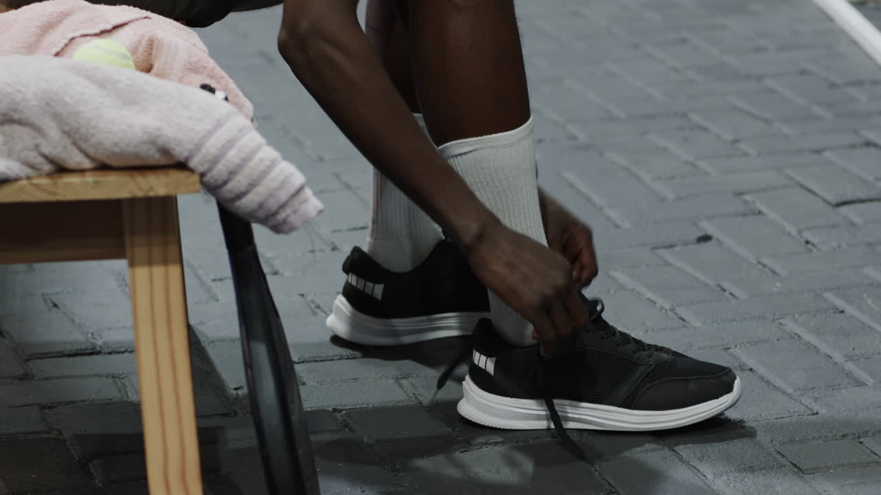 Athlete in orange shirt preparing for padel tennis match, adjusting wristband, on indoor court