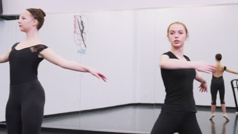 female students at performing arts school rehearsing ballet in dance studio reflected in mirror