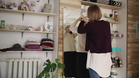 young woman fitting knitted hat front full length mirror in boutique