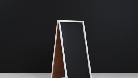 Video-of-blackboard-sign-on-white-stand-with-copy-space-on-black-background