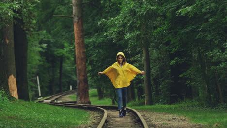 Chica-Encantadora-Con-Un-Impermeable-Amarillo-Corriendo-Y-Caminando-Alegremente-En-El-Viejo-Ferrocarril-En-El-Bosque