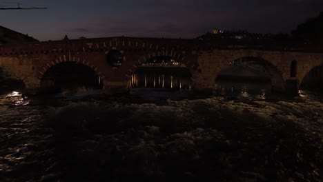 Disparo-Aéreo-De-Un-Dron-Pasando-Por-El-Puente-Ponte-Pietra-En-Verona-Por-La-Noche-Hasta-S