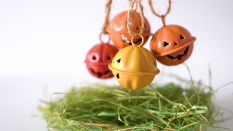 campanas de cabeza de calabazas de halloween de metal ondeando sobre heno verde, colgando de una mano femenina, aisladas en fondo blanco, fondo de promoción creativa