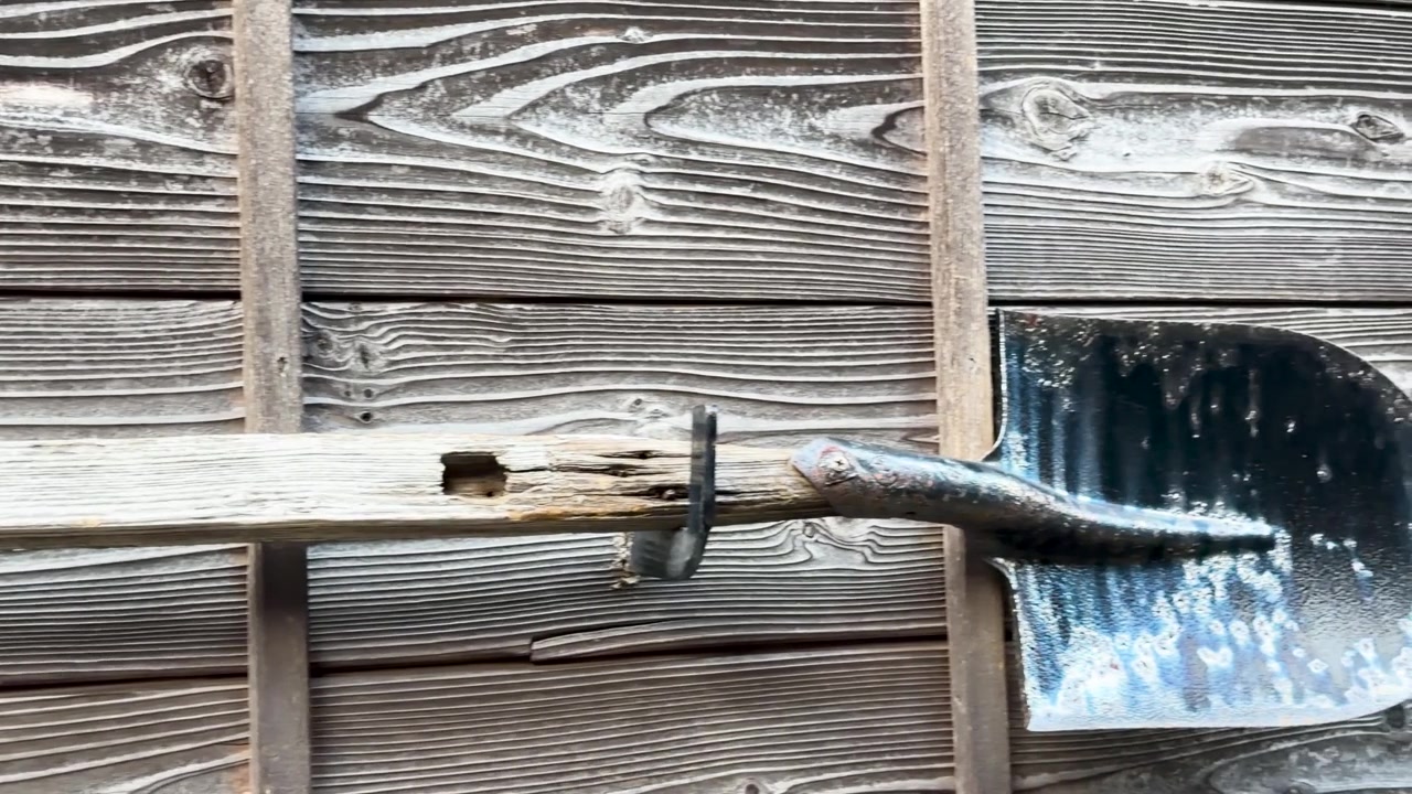 A slow panning shot of a vintage garden spade hanging on an aged wood wall.