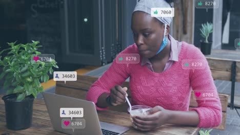 Animation-Von-Social-Media-Symbolen-Mit-Zahlen-über-Einer-Afroamerikanischen-Frau,-Die-Einen-Laptop-Benutzt