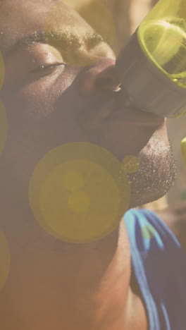 yellow spots of light against close up of african american fit man drinking water