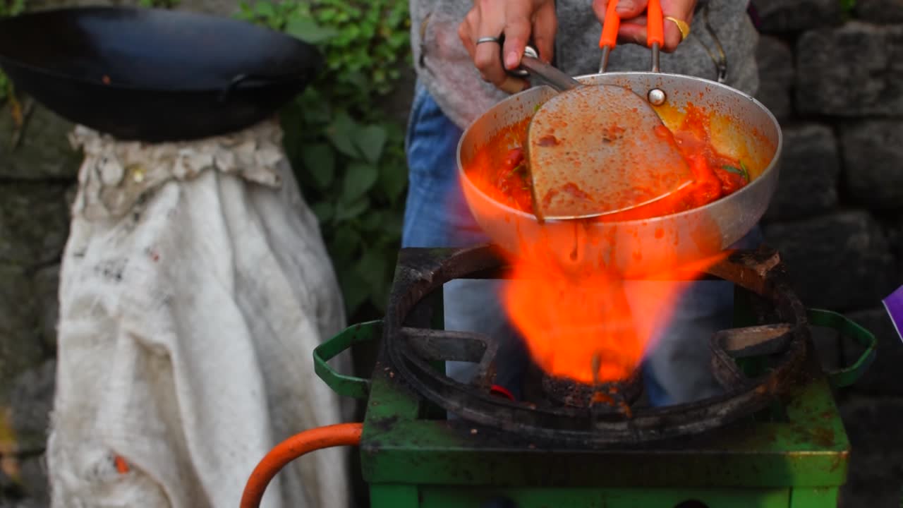 A slow motion shot of a street vendor frying the Chilling chicken in a Pan with lot of fire to sell in the streets of Darjeeling