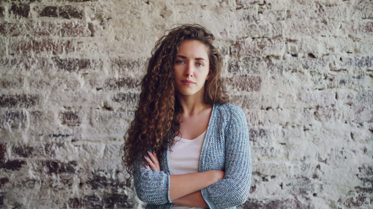 Young Woman with Curly Hair Posing in Front of a Brick Wall