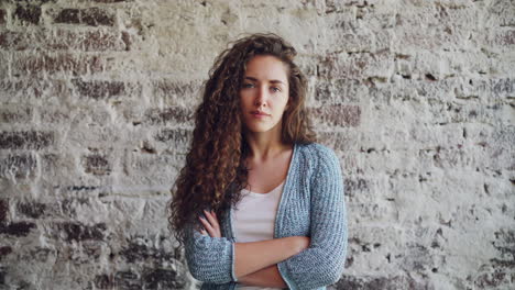 young woman with curly hair posing in front of a brick wall
