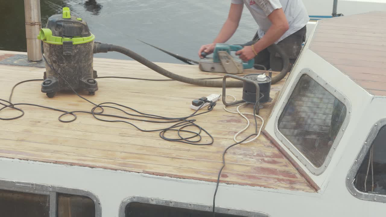Young man removing varnish on forecabin wooden boat roof