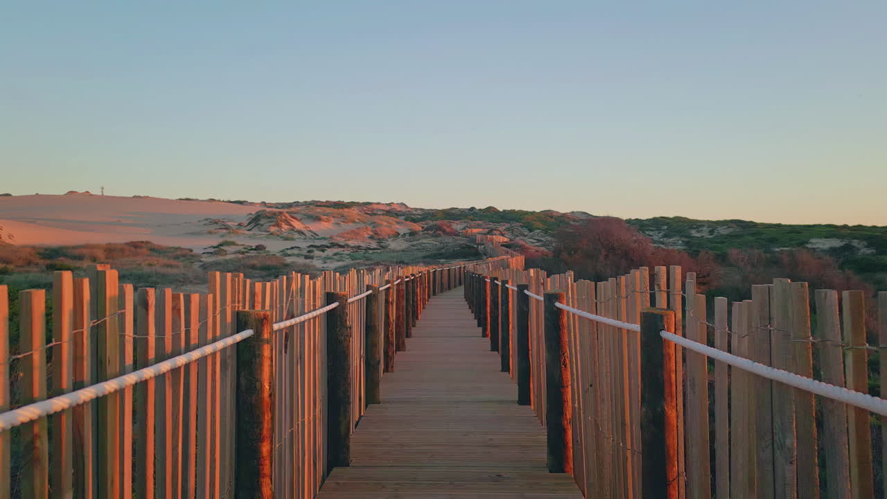 Wooden walkway sunset light lead through vibrant sand dunes. Scenic empty pier
