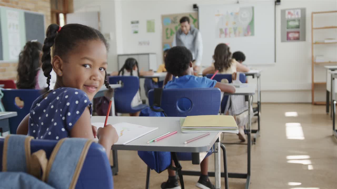 retrato de una niña biracial escribiendo en un escritorio en una clase de escuela primaria diversa, cámara lenta