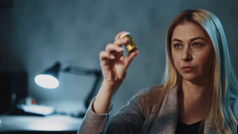 Woman-patient-looks-at-remedy-in-bottle-in-semi-dark-room