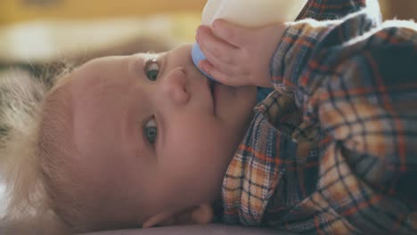 funny baby eats milk mix from plastic bottle lying on bed