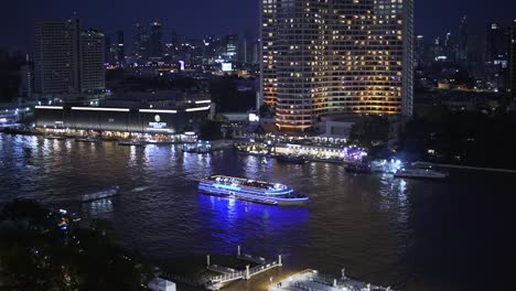 A-scenic-view-of-the-Chao-Phraya-River-at-night-with-bustling-nightlife-and-cruise-boats-passing-by