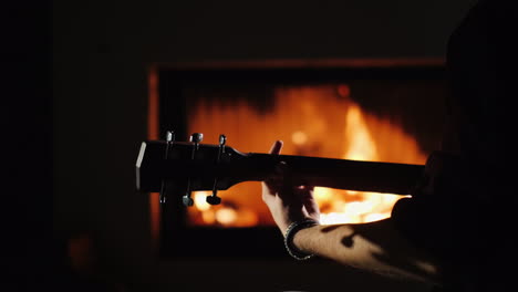 Un-Joven-Toca-La-Guitarra-Sentado-Solo-Junto-A-La-Chimenea