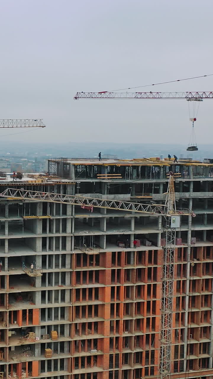 New construction in the city center. Wide high-rise building under construction outdoors. Aerial view. Camera moving around. Vertical video