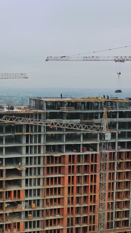 new construction in the city center. wide high-rise building under construction outdoors. aerial view. camera moving around. vertical video