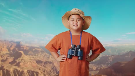 asian boy with a hat and binoculars smiling to camera with arms akimbo while traveling at the top of mountain. boy researcher examines something, travel tourism adventure concept