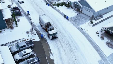 drone shot of a garbage truck picking up trash in the ice cold elements with snow covering the ground