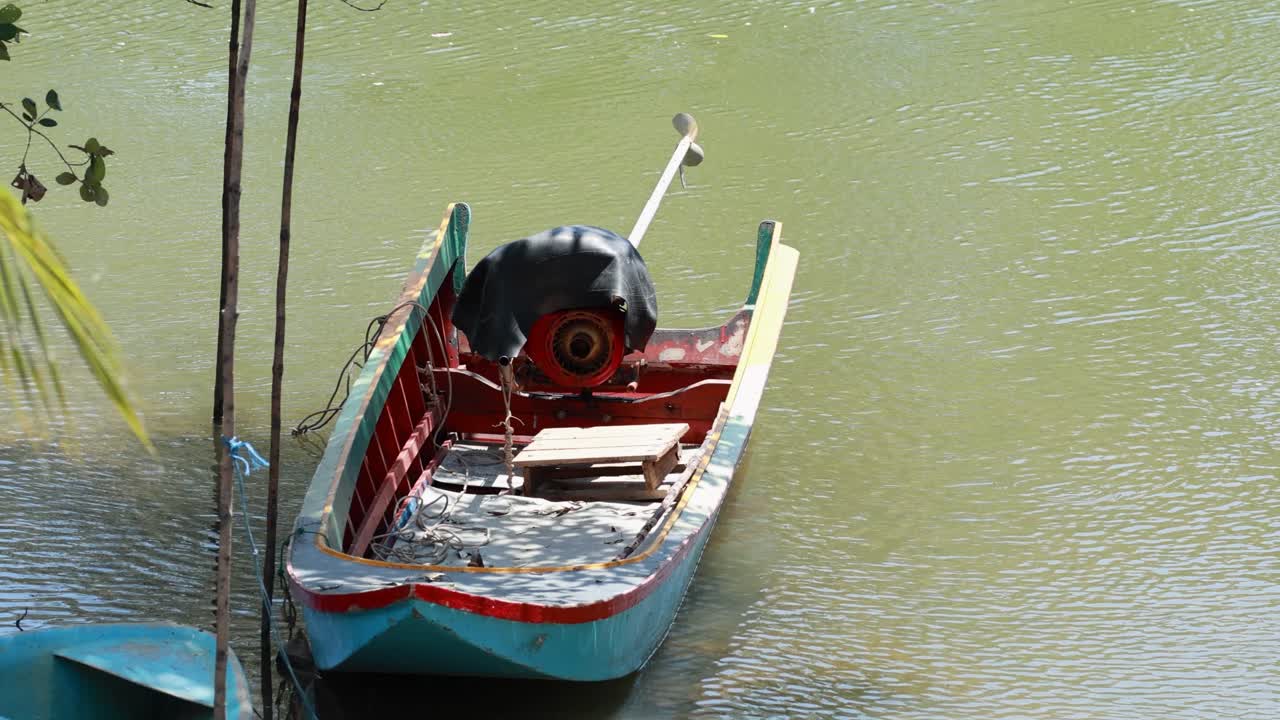 A traditional longtail boat gently floats on calm waters in Phuket, Thailand, under bright daylight