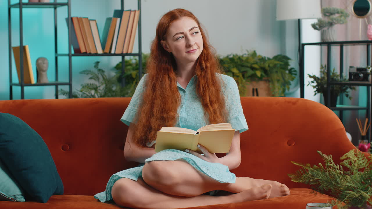 Young woman relaxing interesting book turning pages smiling enjoying literature taking rest on sofa