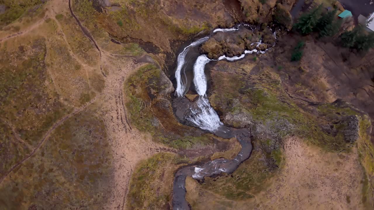 Ripresa drone di una cascata impetuosa in Islanda che si divide in due corsi d'acqua attraverso un paesaggio brullo.