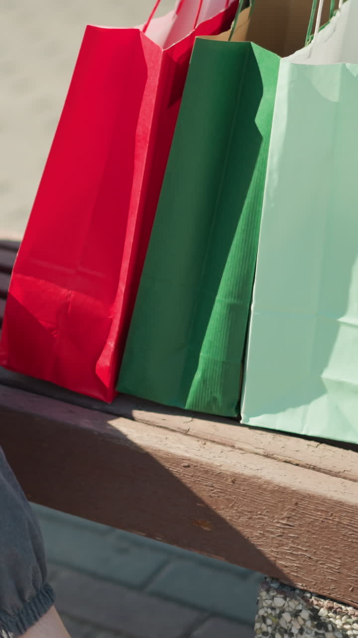 vista de cerca de la pierna de una mujer con corredores grises dejando caer sus bolsas de compras en un banco de madera, ajusta su bolso con la mano izquierda, luego se sienta y cruza su pierna izquierda sobre la pierna derecha