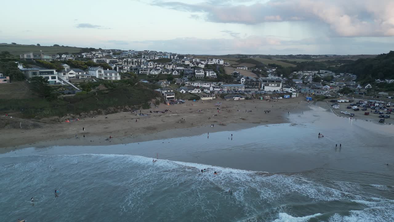 Captivating aerial footage of Polzeath Beach in Cornwall at sunset, showcasing rolling waves, sandy shores, and distant hills under soft evening light. Ideal for coastal and travel themes