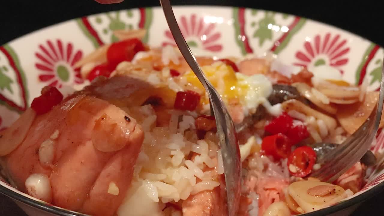 Primo piano di mani che usano un cucchiaio e una forchetta per mescolare salmone e riso