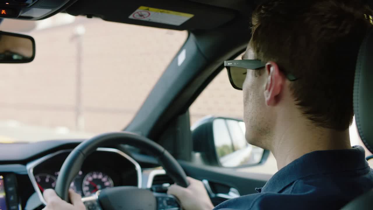 Glancing driver navy shirt sunglasses prompted by sun turning head right, holding wheel