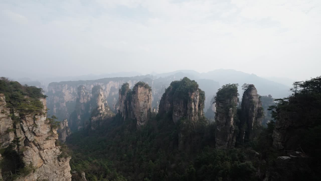 Towering sandstone pillars and dense forest ridges stretch across the misty horizon of Zhangjiajie’s surreal mountain landscape