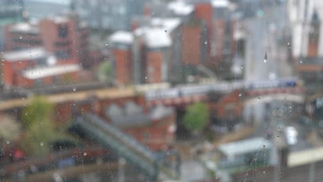 Gotas-De-Lluvia-En-La-Ventana,-Tren-Cruzando-La-Ciudad-En-Segundo-Plano