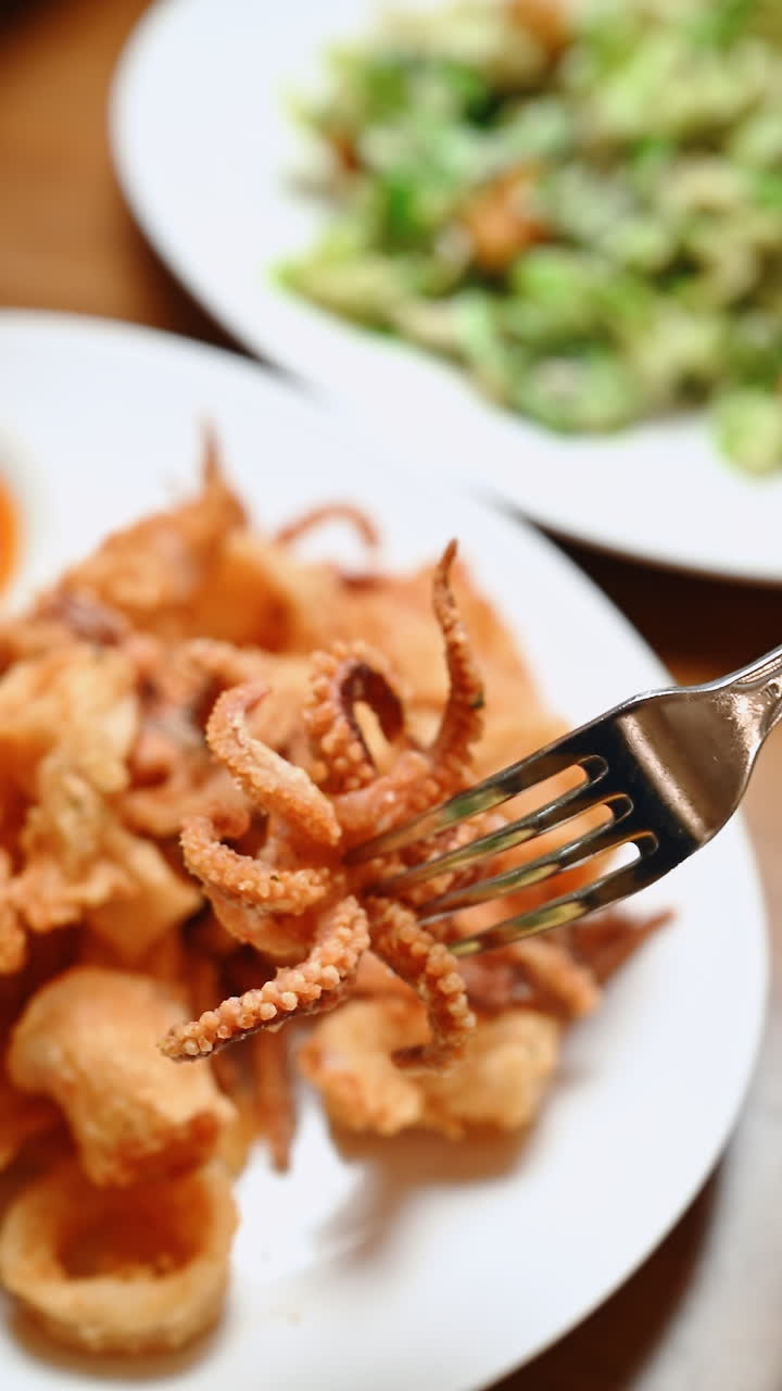 Calamari fritti serviti con insalata in un ristorante di sera. Calamari fritti vengono presi con una forchetta mentre l'insalata è su un piatto nelle vicinanze in un ristorante