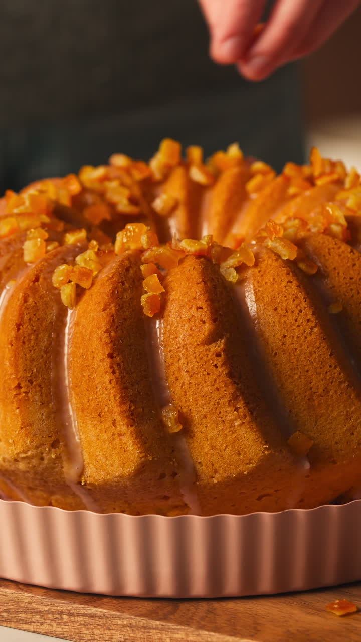 Hand Sprinkling Candied Fruit Pieces On Top Of Golden-Brown Bundt Cake. - vertical. closeup shot