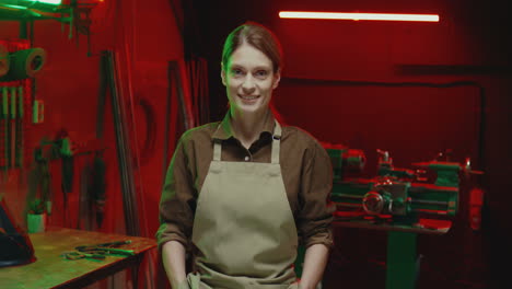 portrait of young woman in apron smiling at camera in metal workshop