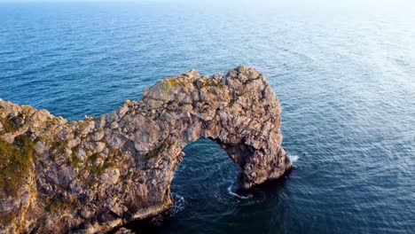 a steady panning shot filmed with a dji mavic of the famous, 'durdle door' during golden hour along the jurassic coastline of britain, with the calm sea in the back ground